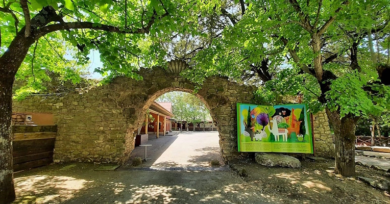 Ein steinerner Bogen zwischen den Bäumen führt in einen Freizeitpark; auf seiner rechten Seite erzählt ein riesiges Buch die Geschichte des Parks.