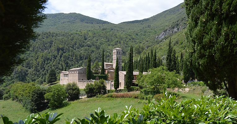 L'Abbazia di San Pietro in Valle immersa nel verde, circondata da cipressi e colline boscose.