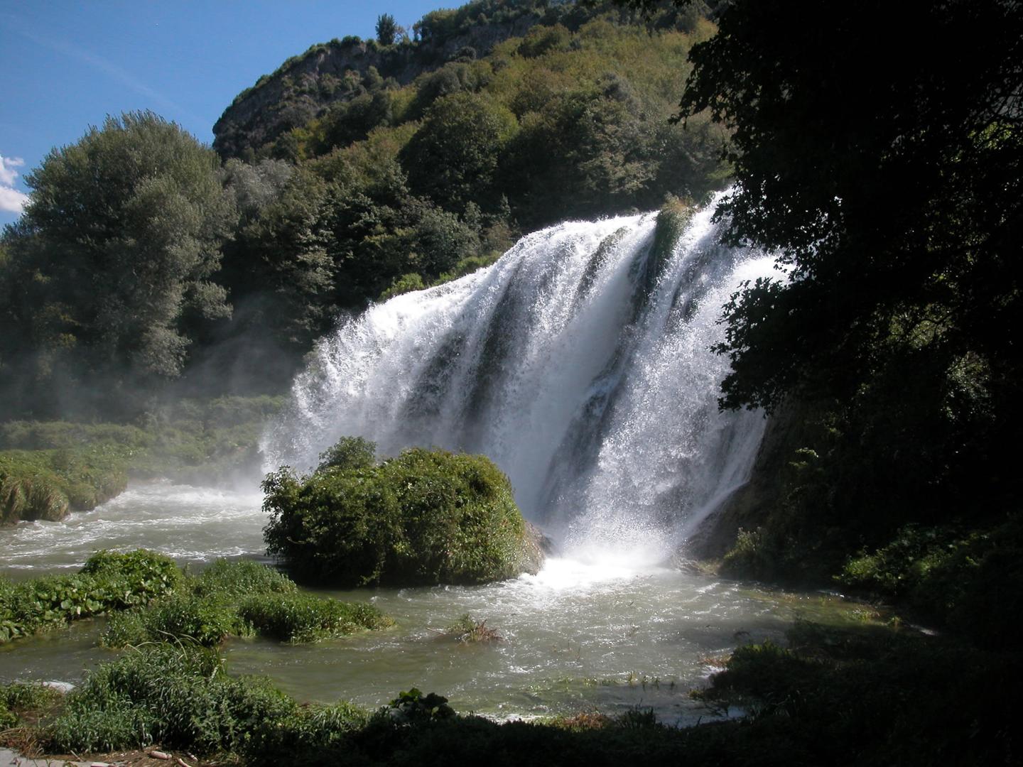 Cascata delle Marmore vista laterale: il flusso d’acqua si infrange su rocce circondate da vegetazione rigogliosa e alberi.