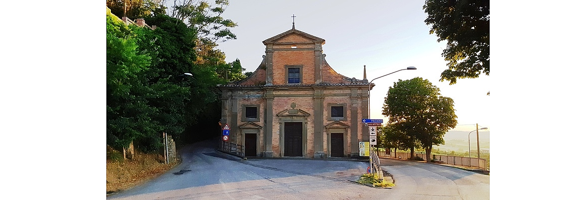 Una piccola chiesa in mattoni, circondata da alberi, si trova a un bivio con cartelli stradali.