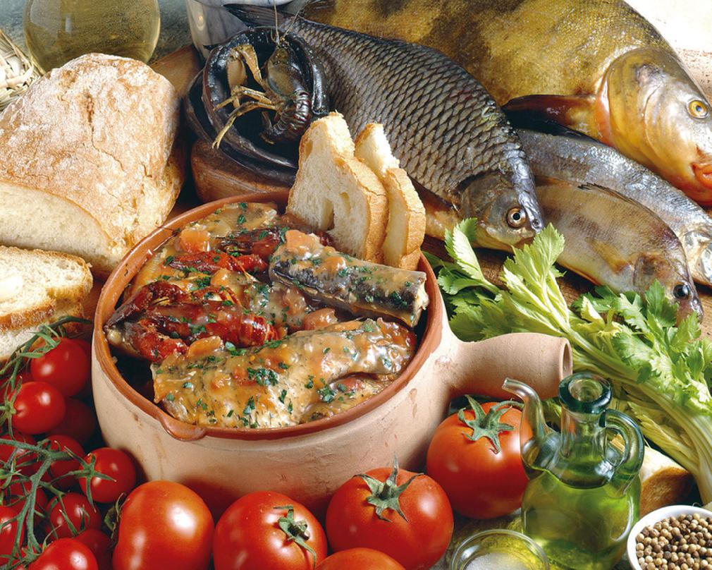 Plat de poisson de lac mijoté avec tomates, persil et pain, entouré d'ingrédients frais et de poissons entiers.