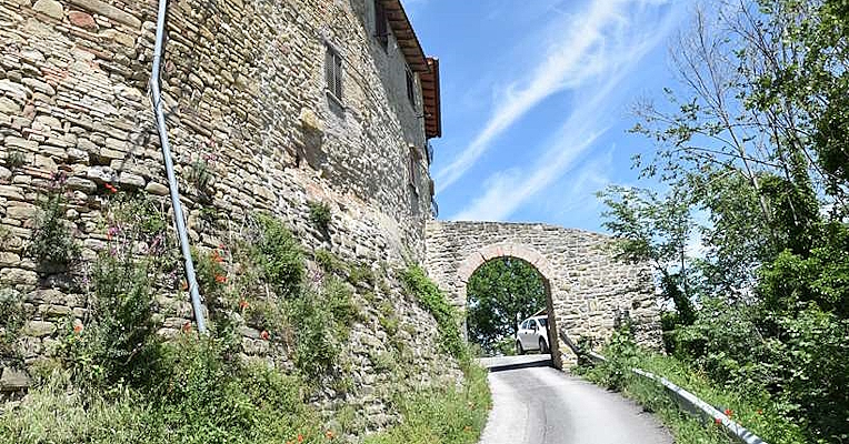 Entrance to the fortified village of Castel d’Arno, with a road passing under a stone arch between the walls of the medieval castle.