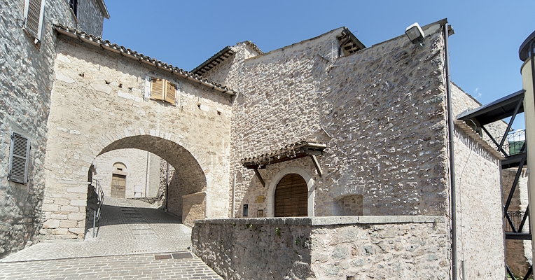 Vicolo acciottolato con arco in pietra e edifici storici, immerso nel centro storico di Cerreto di Spoleto.