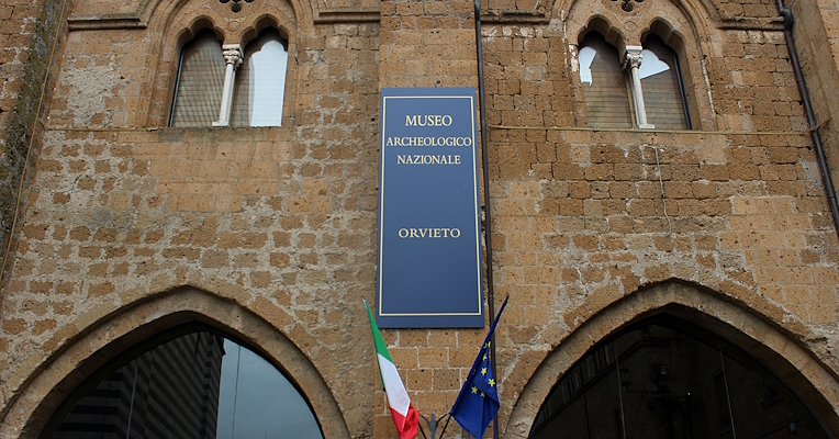 Eingang mit Flaggen und einem blauen Banner mit der goldenen Aufschrift „Museo Archeologico Nazionale“ – Orvieto