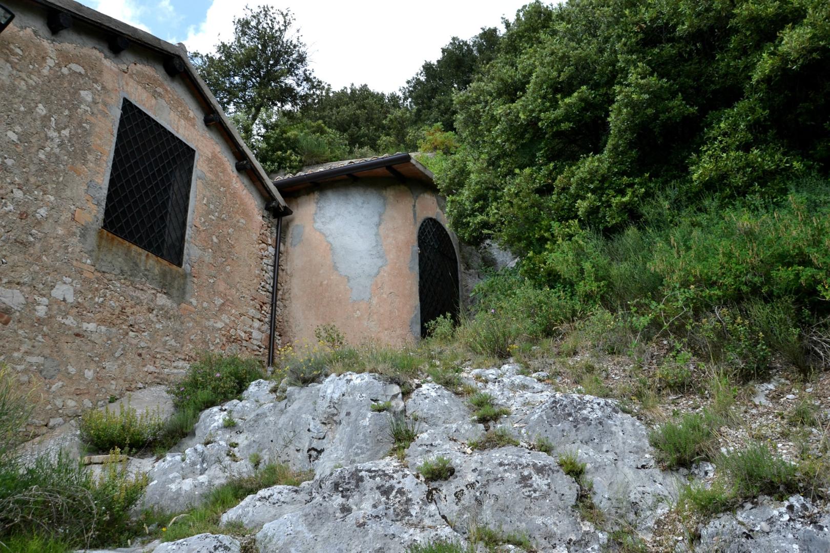Esterno in pietra dell’Eremo della Madonna del Riparo, con mura e finestre grate, immerso nel verde e nella roccia.