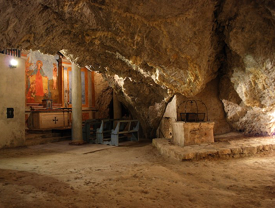 Interior of the cave of the Hermitage of Madonna del Riparo with frescoed altar, wooden benches and ancient stone well.