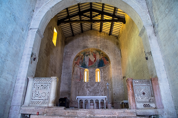 Interior of a Romanesque church with apse frescoes, wooden ceiling, and decorated marble screens.