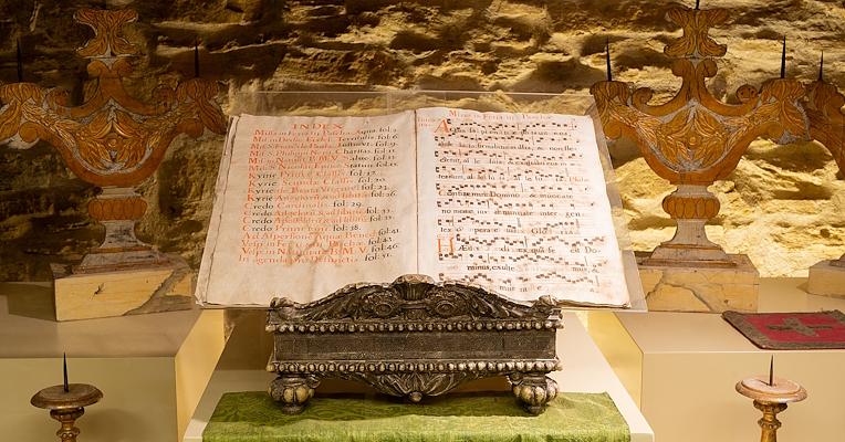 Un leggio antico con spartiti che riportano cantici liturgici, con note ben visibili e usurati dal tempo.