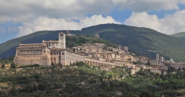 Vista panoramica di Assisi con la Basilica di San Francesco in primo piano ed edifici storici. Sullo sfondo il Monte Subasio