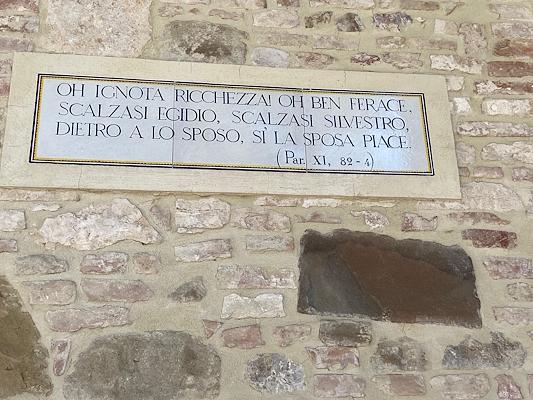 A marble plaque with a Dantean inscription embedded in a stone and brick wall, featuring a quote from Paradiso.