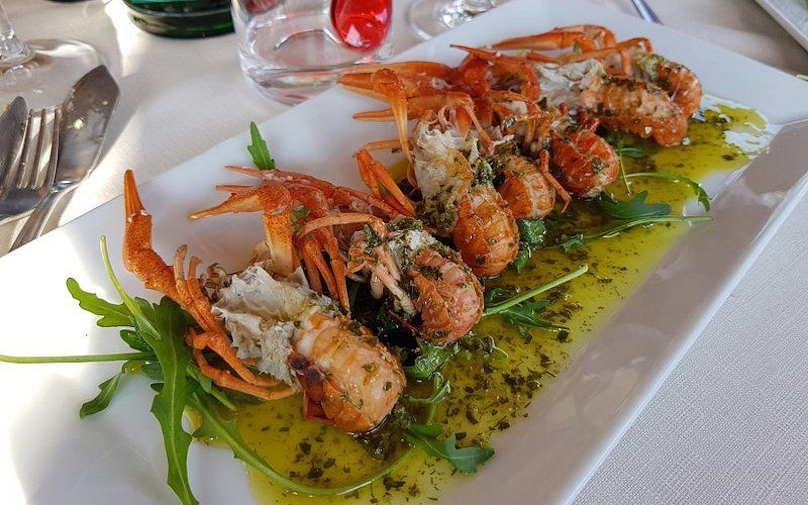 Flusskrebse auf Rucolabett mit grüner Kräutersoße, elegant serviert auf weißer Platte im Restaurant. (Photo credits: TRATTORIA TERESA)