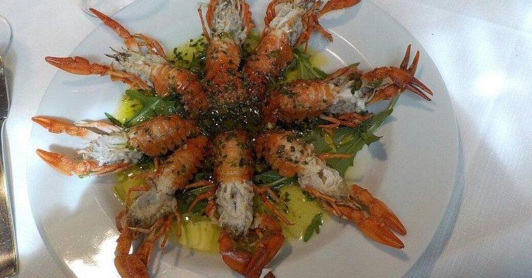 Flusskrebse sternförmig auf weißem Teller angerichtet, mit grüner Soße und Rucola.