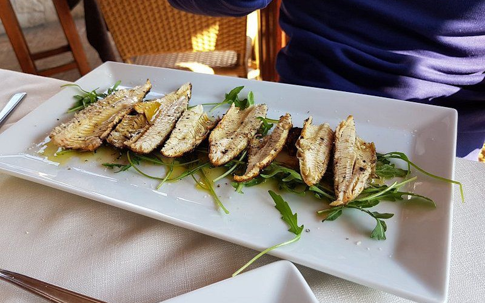 Gegrillte Süßwasserfischfilets (Carbonaretti), auf Rucolabett mit Olivenöl extra vergine, angerichtet auf weißer Platte. (Photo credits: TRATTORIA TERESA)