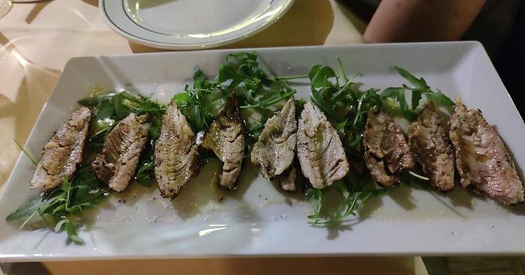 Gegrillte Süßwasserfischfilets auf Rucolabett mit Öl und Pfeffer, ordentlich auf rechteckiger weißer Platte serviert.
