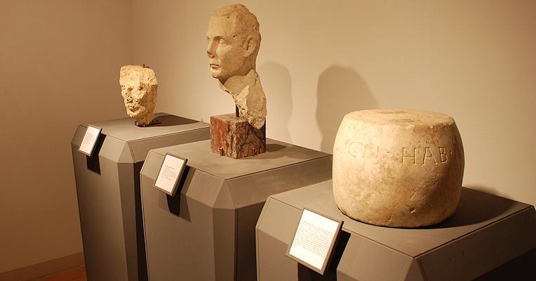 Deux bustes en pierre et un objet cylindrique avec une inscription latine, exposés sur des socles avec des légendes