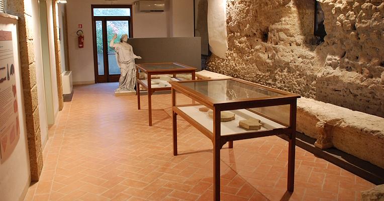 Spazio espositivo di un museo archeologico con vetrine contenenti reperti, una statua in fondo alla stanza