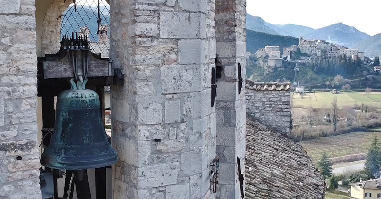 Bronzeglocke in einem steinernen Glockenturm, mit einer mittelalterlichen Burg im Hintergrund