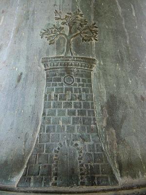 Bassorilievo su campana di bronzo raffigurante una torre in pietra sormontata da un albero di ulivo stilizzato.