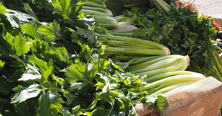 Celery stalks with leaves on a burlap-covered stall at an open-air market