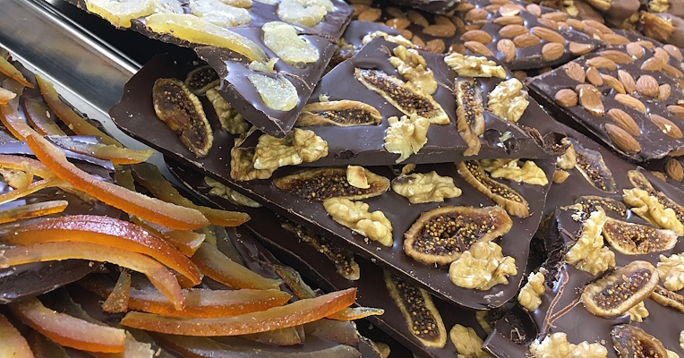 Dark chocolate bars topped with dried figs, walnuts, almonds, and candied orange and ginger peels, displayed on a counter.