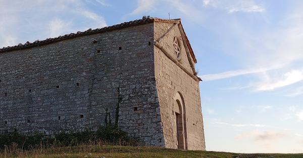  Vue latérale d’un bâtiment en pierre situé sur une colline herbeuse, avec un ciel bleu et de légers nuages en arrière-plan. 