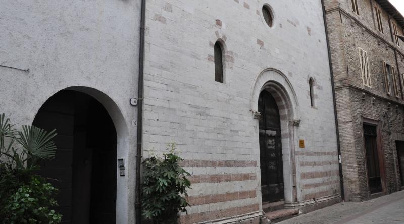 Facciata in pietra della chiesa di San Biagio a Cannara, con portale ad arco e piccole finestre, affacciata su una via.