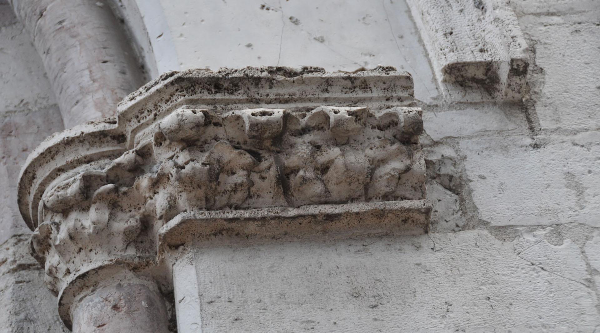 Dettaglio di un capitello scolpito in pietra, con motivi decorativi consumati dal tempo, sulla facciata della chiesa.