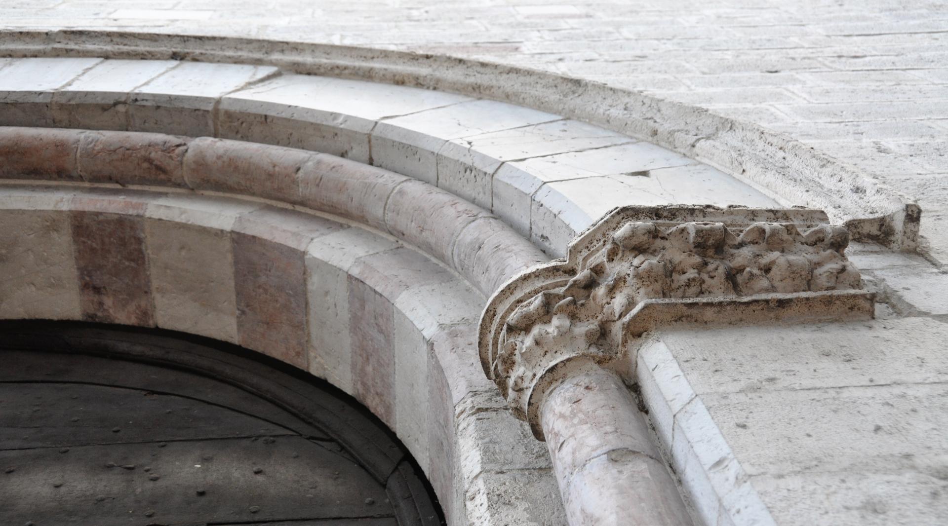 Dettaglio del portale ad arco in pietra della chiesa, con capitello scolpito e decorazioni consumate dal tempo.