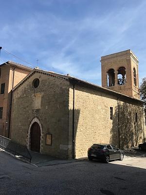 View of the Church of Sant’Agostino in Gualdo Cattaneo, with its stone façade and bell tower standing out against the sky.