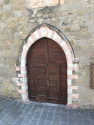 Wooden portal of the Church of Sant’Agostino in Gualdo Cattaneo, framed by a two-tone stone Gothic arch.