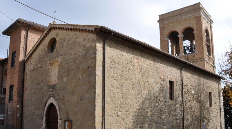 Église en pierre à la façade simple et au clocher en briques, vue latéralement sous un ciel nuageux.