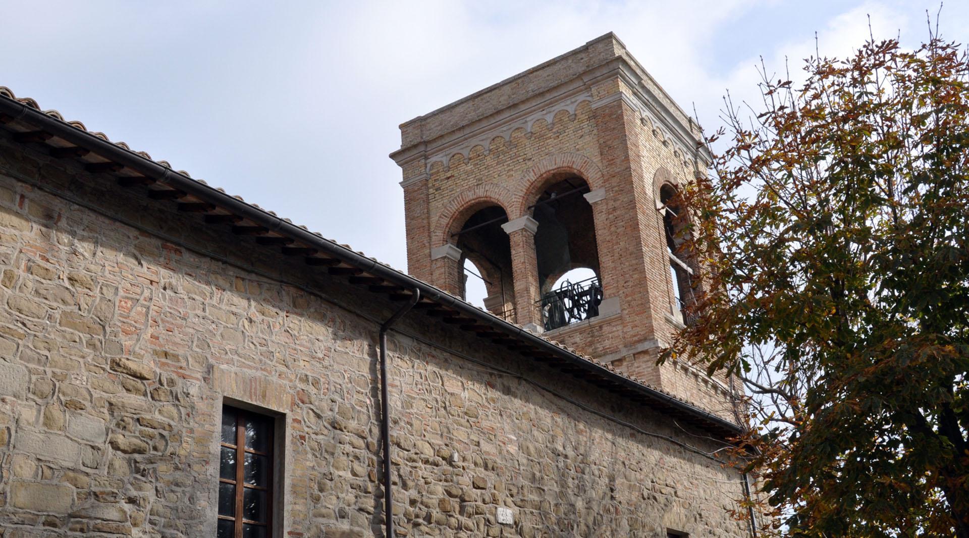 Stone church with a simple façade and a brick bell tower, seen from the side under a cloudy sky.