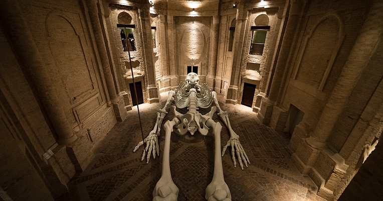 Art installation of a giant skeleton lying inside a brick-arched chapel.