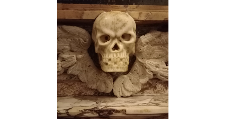 Marble-carved skull with decorative wings, part of a funeral monument.
