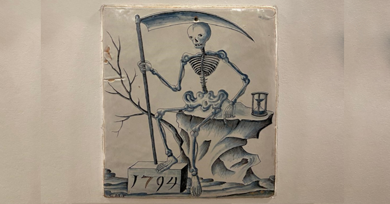  1794 ceramic illustration of a skeleton with a scythe sitting on a rock next to an hourglass. 
