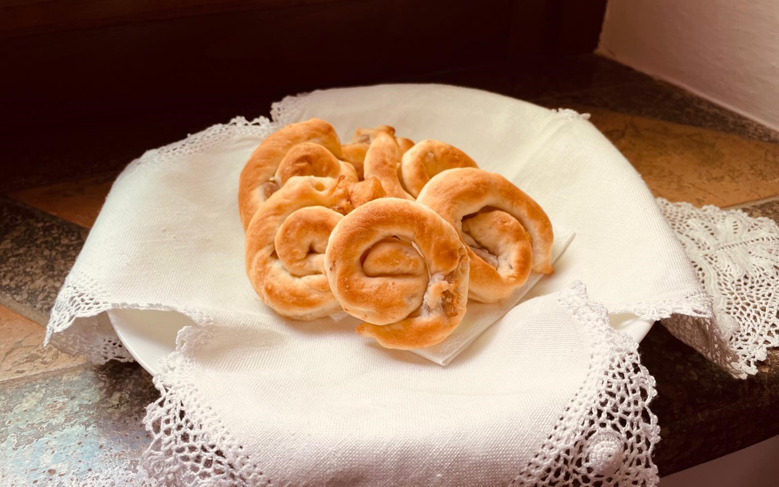 Plate of snail-shaped lumachelle from Orvieto, arranged on a white lace napkin placed on a stone windowsill.
