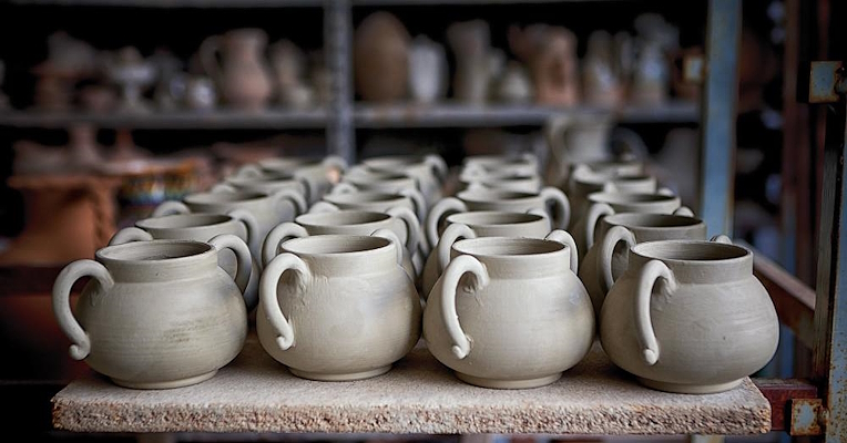 Rangées de pots en terre cuite non émaillés, soigneusement disposés sur une étagère dans un atelier de céramique.