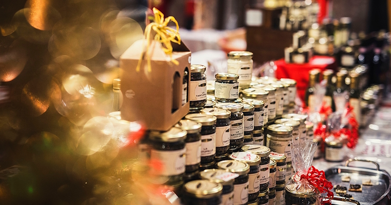 Display of handcrafted and gastronomic products on a Christmas stall inside the Rocca Paolina in Perugia, decorated with red ribbons and warm lights.