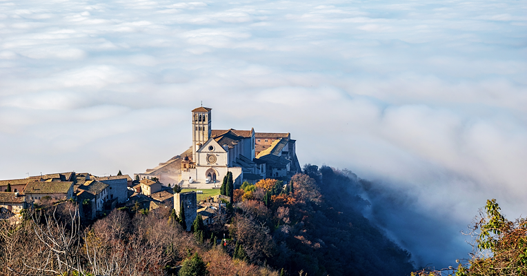 Das Umbra-Tal, eingehüllt in Winternebel, und die Basilika des Heiligen Franz von Assisi, die im Sonnenlicht hervorsticht.