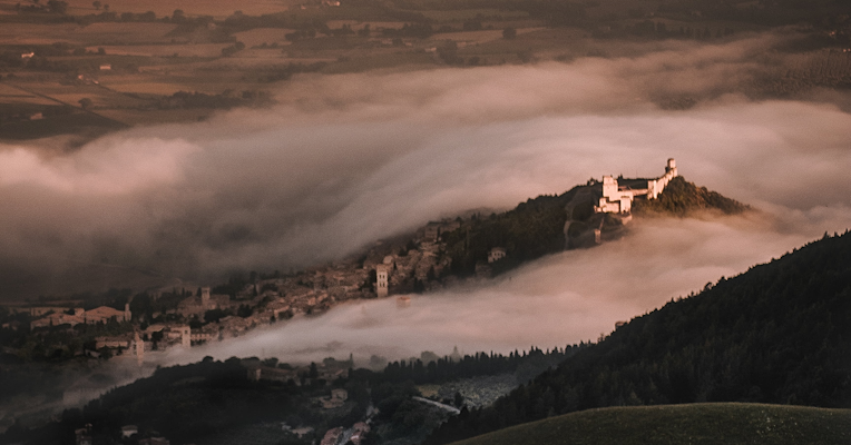 Das Umbra-Tal, eingehüllt in Winternebel, und die Basilika des Heiligen Franz von Assisi, die im Sonnenlicht hervorsticht.