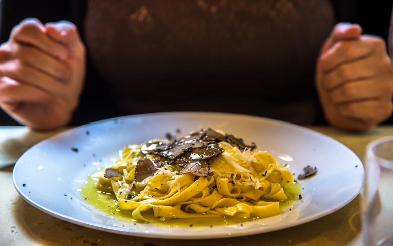 Immagine: Plate of tagliatelle with truffle shavings, with hands resting on the table ready to eat in the background. 