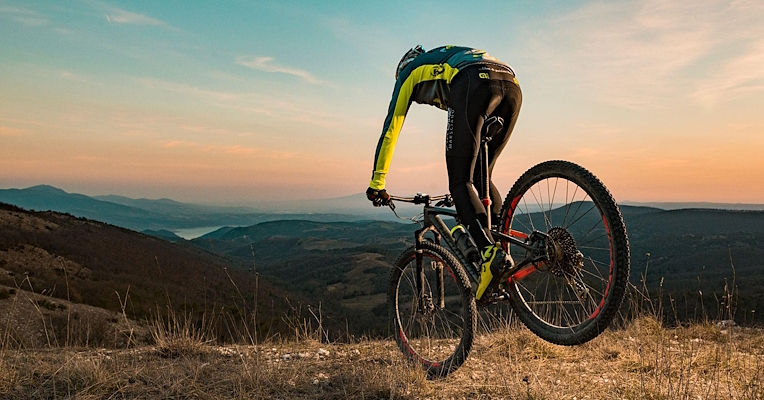  Ciclista in mountain bike su sentiero collinare con panorama di montagne al tramonto 