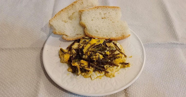  Uova strapazzate con asparagi selvatici servite su piatto bianco con fette di pane casereccio. 