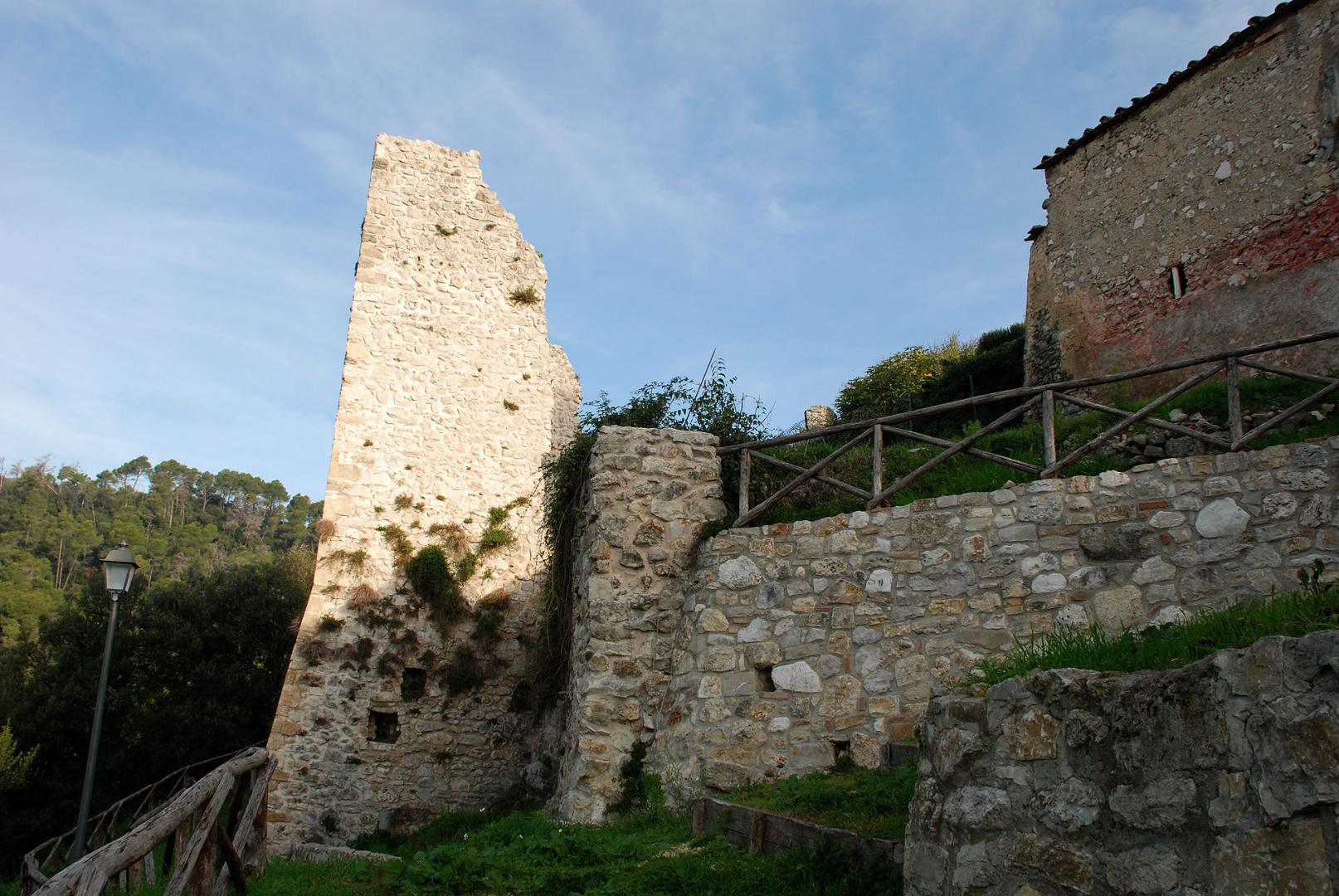 Rovine del Castello di Poggio di Otricoli: resti di una torre in pietra tra mura antiche, vegetazione e cielo limpido.