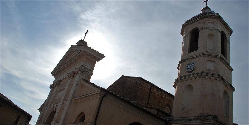 Façade et clocher de la collégiale Santa Maria Assunta à Otricoli, en contre-jour sous un ciel voilé.