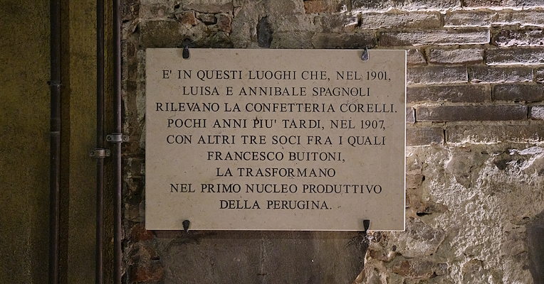 Targa commemorativa in pietra su muro in mattoni che racconta la nascita della Perugina nei primi anni del Novecento.