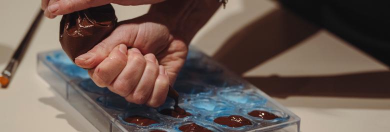 Immagine: Hands filling a transparent mould with melted chocolate using a piping bag. 