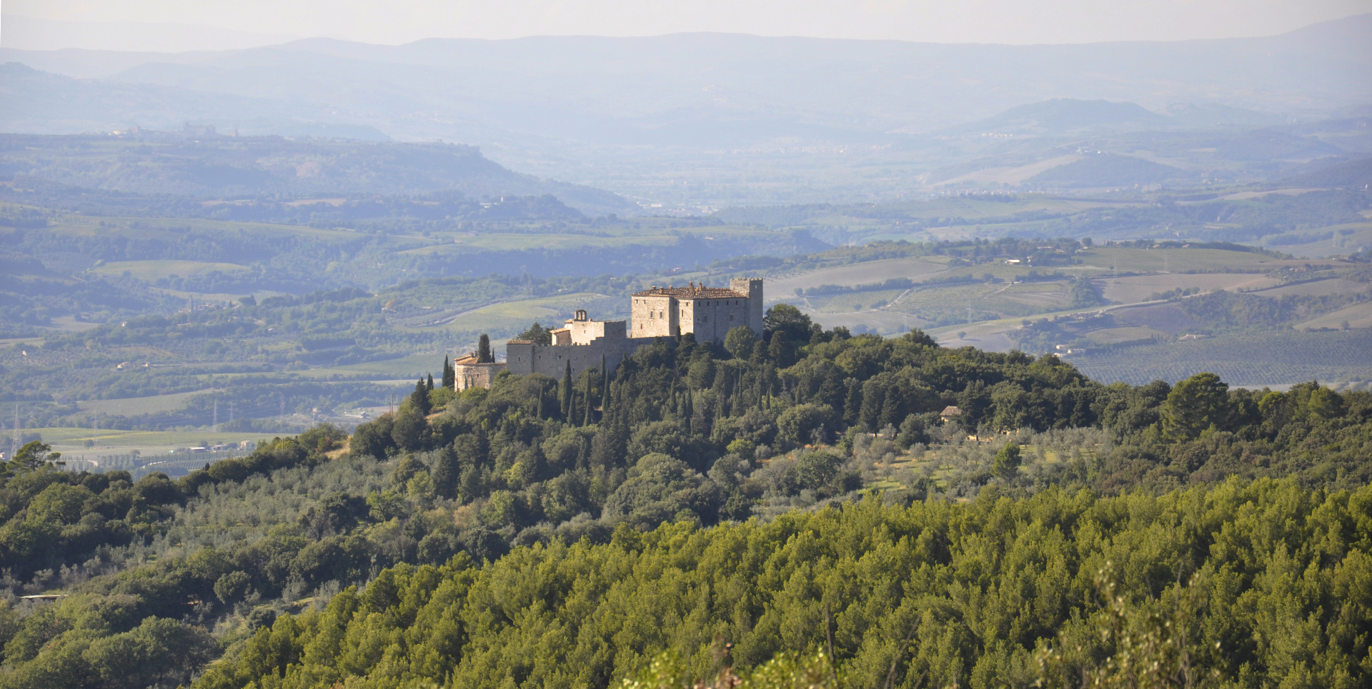 Veduta panoramica del Castello del Poggio immerso nel verde delle colline umbre, con paesaggio collinare sullo sfondo.