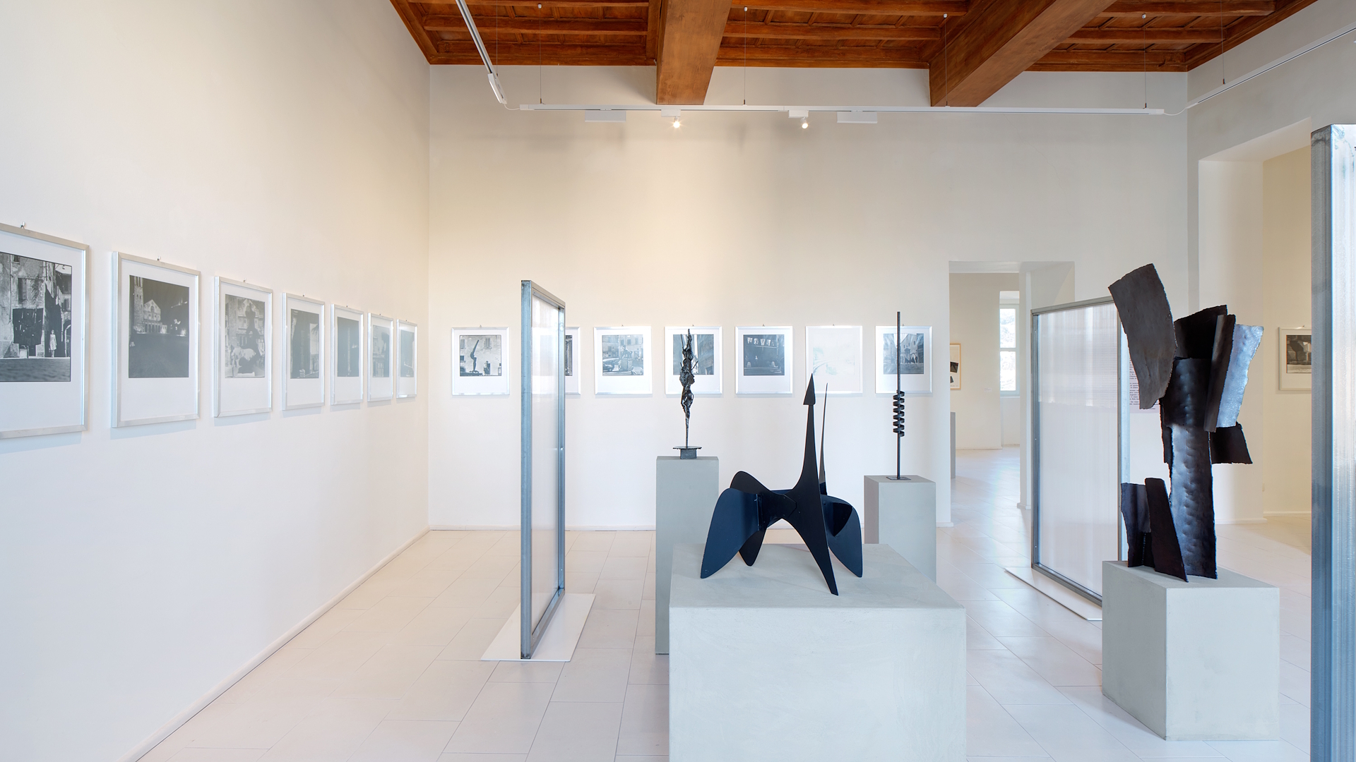 Exhibition room at Palazzo Collicola with contemporary sculptures and photographs on the walls.