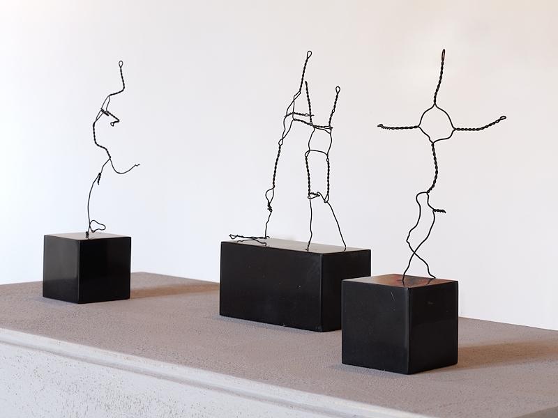Tre sculture filiformi in ferro raffiguranti figure umane stilizzate in diverse pose, esposte su basi nere.